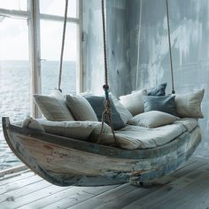 a wooden swing bed hanging from a wall next to a window with water in the background