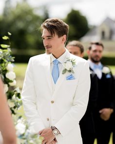 a man wearing a white suit and blue tie standing next to another man in a wedding dress