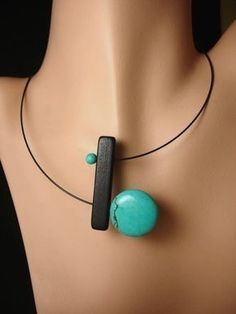 a necklace with a turquoise stone and black bead hangs on a mannequin's neck