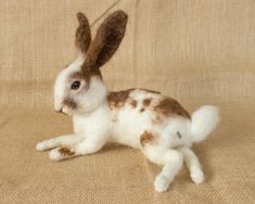 a brown and white stuffed rabbit sitting on top of a tan cloth covered floor next to a wall