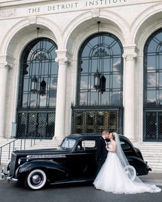 a bride and groom are standing in front of an old car outside the detroit institution