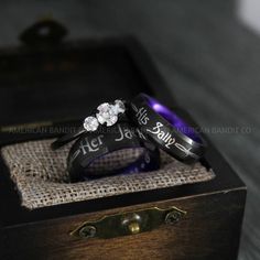 two wedding rings sitting on top of each other in a wooden box with the words his and hers written on them