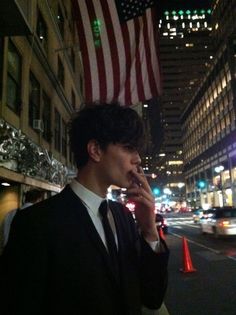 a man in a suit and tie talking on a cell phone with an american flag hanging over his head