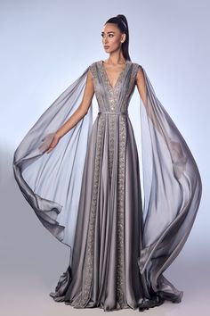 Indulge in the epitome of elegance with the Reverie Couture FW46 Beaded Mouseline Gown. Intricately handcrafted beadwork adorns the delicate fabric, exuding sophistication and charm. The floor-length skirt flows gracefully, while the matching clutch adds the perfect finishing touch. Elevate your evening attire with this stunning ensemble. Silver Medieval Dress, Daenerys Targaryen Dress, Princess Story, Gown With Cape, Fantasy Outfits, Dress Cape, Silver Gown, Cape Sleeves, Floor Length Skirt