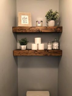 two wooden shelves above a toilet in a bathroom with candles and plants on the shelf