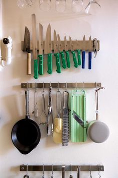 kitchen utensils hanging on the wall above pots and pans with knives attached to them