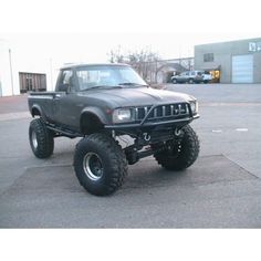 a gray truck parked in a parking lot next to a large black tire on top of it's tires