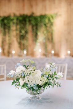 a vase filled with white and blue flowers on top of a table next to chairs