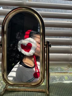 a woman wearing a red and white knitted hat is reflected in a mirror with blinds