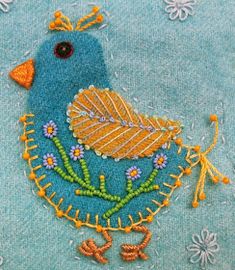 a blue bird with yellow feathers and flowers on it's back is embroidered onto the fabric