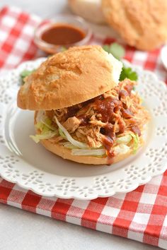 a pulled pork sandwich on a bun with lettuce and tomato sauce sitting on a white plate