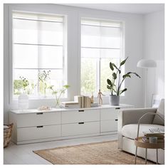 a living room with white furniture and plants in the window sill, along with a rug on the floor