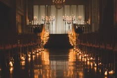 an aisle lined with chairs and candles in front of a chandelier filled with lit candles