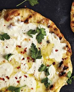 two pizzas with cheese and herbs on them sitting on a black surface next to each other