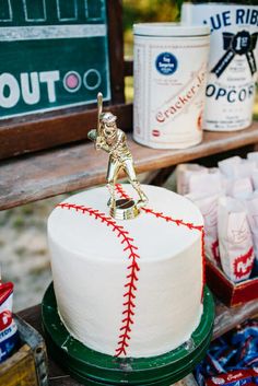 a baseball themed cake on a table with candy and other items in the back ground