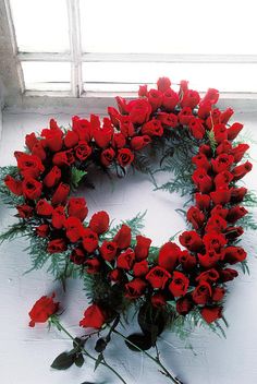 a wreath made out of red flowers on a white wall with windowsills in the background