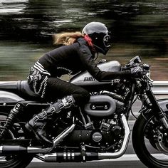 a woman riding on the back of a motorcycle down a road with trees in the background