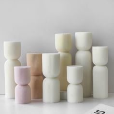 several different colored vases sitting next to each other on a white surface with the number six in front of them