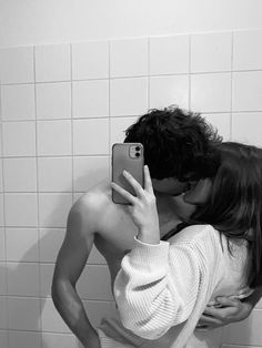 a man and woman kissing in the bathroom while taking a selfie on their cell phone