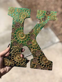 the letter k is decorated with gold and green designs on it's sides, while being held up by a hand