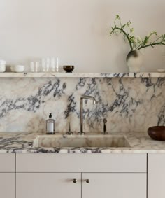 a kitchen with marble counter tops and white cupboards next to a vase filled with flowers