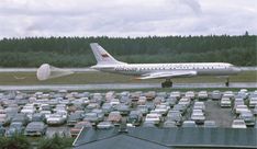 an airplane is parked in a parking lot with lots of cars behind it and trees on the other side