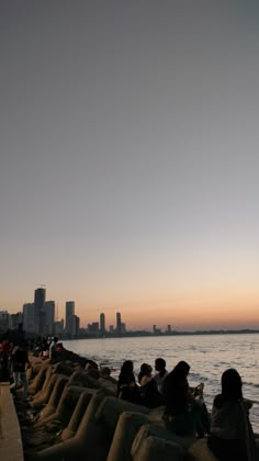 people are sitting on the edge of a wall by the water at sunset or dawn