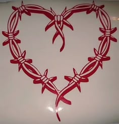 a heart made out of barbed wire on top of a white table with red ribbon