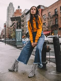 a woman sitting on top of a fire hydrant wearing high heeled shoes and a yellow sweater