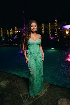 a woman standing in front of a pool at night wearing a green dress with sequins