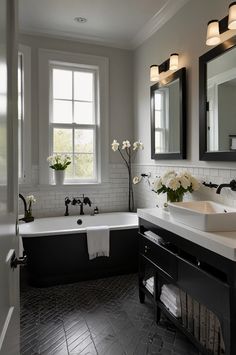 a black and white bathroom with two sinks, tub, mirror and flowers on the counter