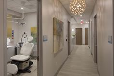 an empty hospital hallway with chairs and lights on either side of the corridor, leading to another room