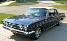 an old car is parked on the sidewalk in front of some grass and trees,