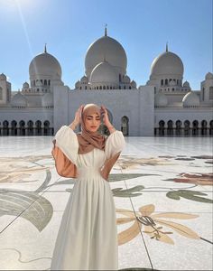 a woman wearing a hijab standing in front of a building with arches and domes