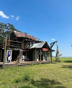 an old wooden building sitting on top of a lush green field next to a metal sculpture