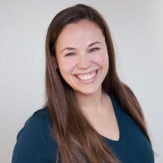 a smiling woman with long brown hair and blue shirt in front of a white wall