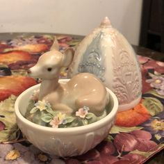 a small deer figurine sitting in a bowl on a table next to an egg