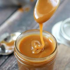 a spoon pouring caramel sauce into a jar on a wooden table with the words super easy caramel sauce