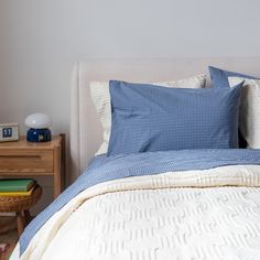 a bed with blue and white pillows on top of it next to a night stand