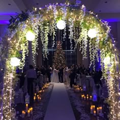 an archway decorated with white flowers and greenery is lit up for a wedding ceremony