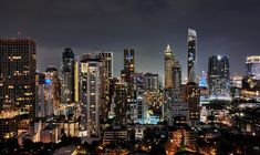 the city skyline is lit up at night with skyscrapers in the foreground and other high rise buildings