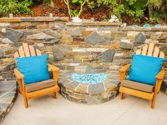 two chairs sitting next to each other in front of a stone wall and fire pit