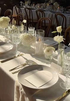 the table is set with white flowers and silverware