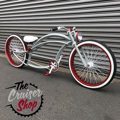 a silver and red tricycle parked in front of a garage door with the words the cruiser shop written on it