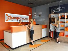 two women are standing at the front desk of an orangetheory store, which is open for business