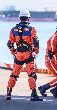 two men in orange and black uniforms are on the tarmac with one man wearing safety gear