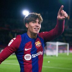 a young man in a red and blue soccer uniform is giving the peace sign with his right hand