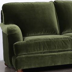 a green couch sitting on top of a hard wood floor next to a white wall