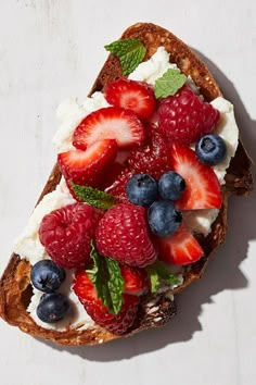 a piece of bread with fruit on top and whipped cream, sitting on a white surface