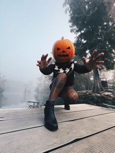 a person dressed as a jack - o'- lantern sitting on a dock with their hands in the air